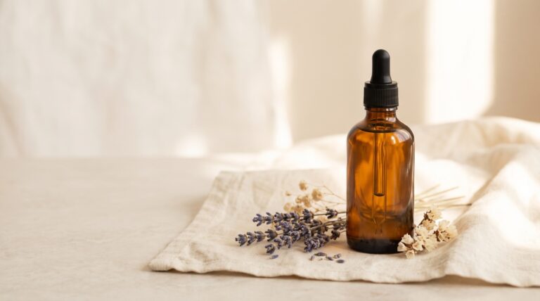 Amber glass bottle of botanical body oil beside dried florals on cream linen, essential oils as perfume, Piton Noir Botanicals Boston
