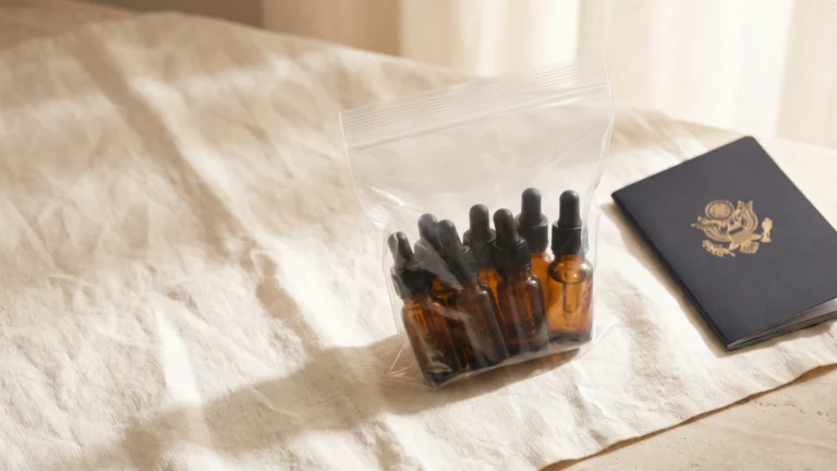 Amber oil bottles in a clear quart bag beside a passport on linen, essential oils on a plane, Piton Noir Botanicals Boston